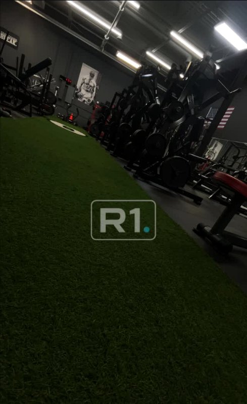 The R1 training floor in Troy: turf runway lined with racks, dumbbells, and strength equipment