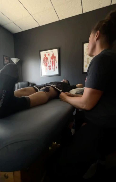 Hands-on treatment in an R1 therapy room, with anatomy charts on the wall